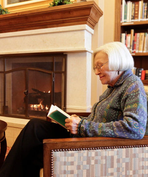 A woman reads by the fireplace at Vi at Highlands Ranch.